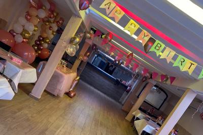 Salle spacieuse avec sol en parquet, murs en pierre et poutres blanches apparentes, éclairée par des lumières modernes.