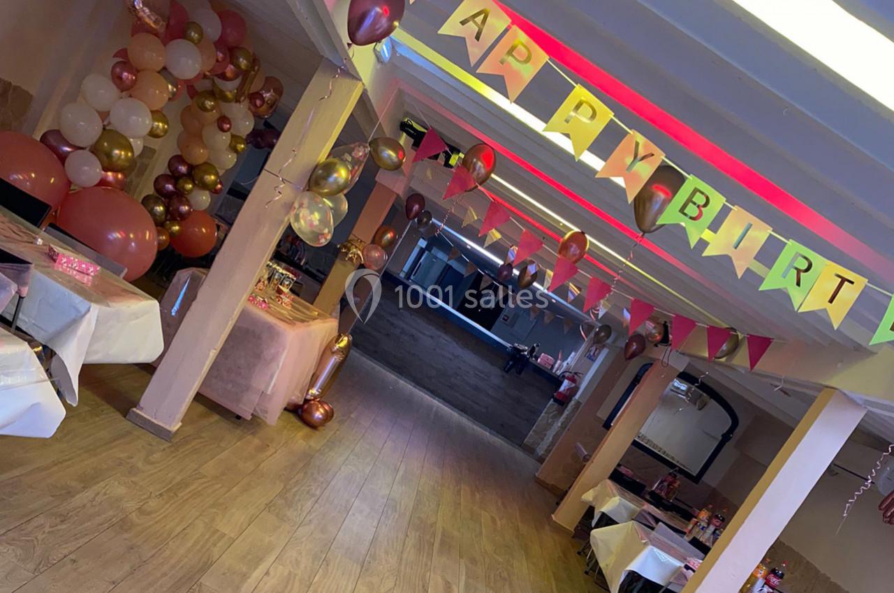 Salle décorée pour un anniversaire avec des ballons, des guirlandes colorées et des tables dressées.