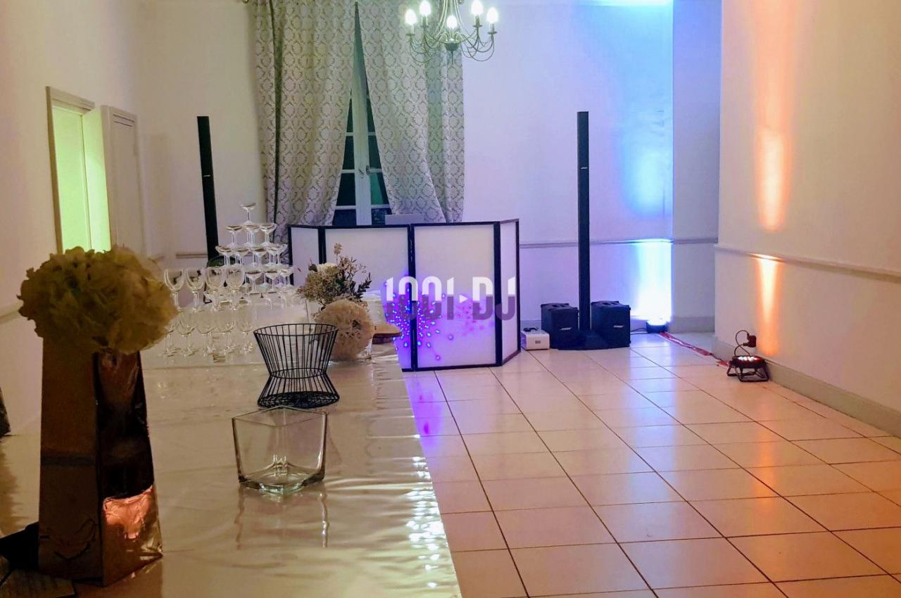 Salle de réception avec décoration lumineuse, table en verre, pyramide de coupes et équipement de sonorisation.