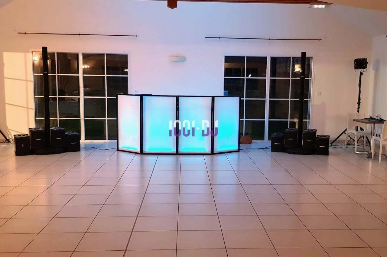 Console de DJ éclairée en bleu et blanc, entourée de haut-parleurs, dans une salle lumineuse avec carrelage clair.