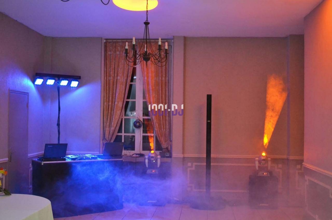 Salle équipée pour un événement avec jeux de lumière, table de mixage et fumée diffusée au sol.