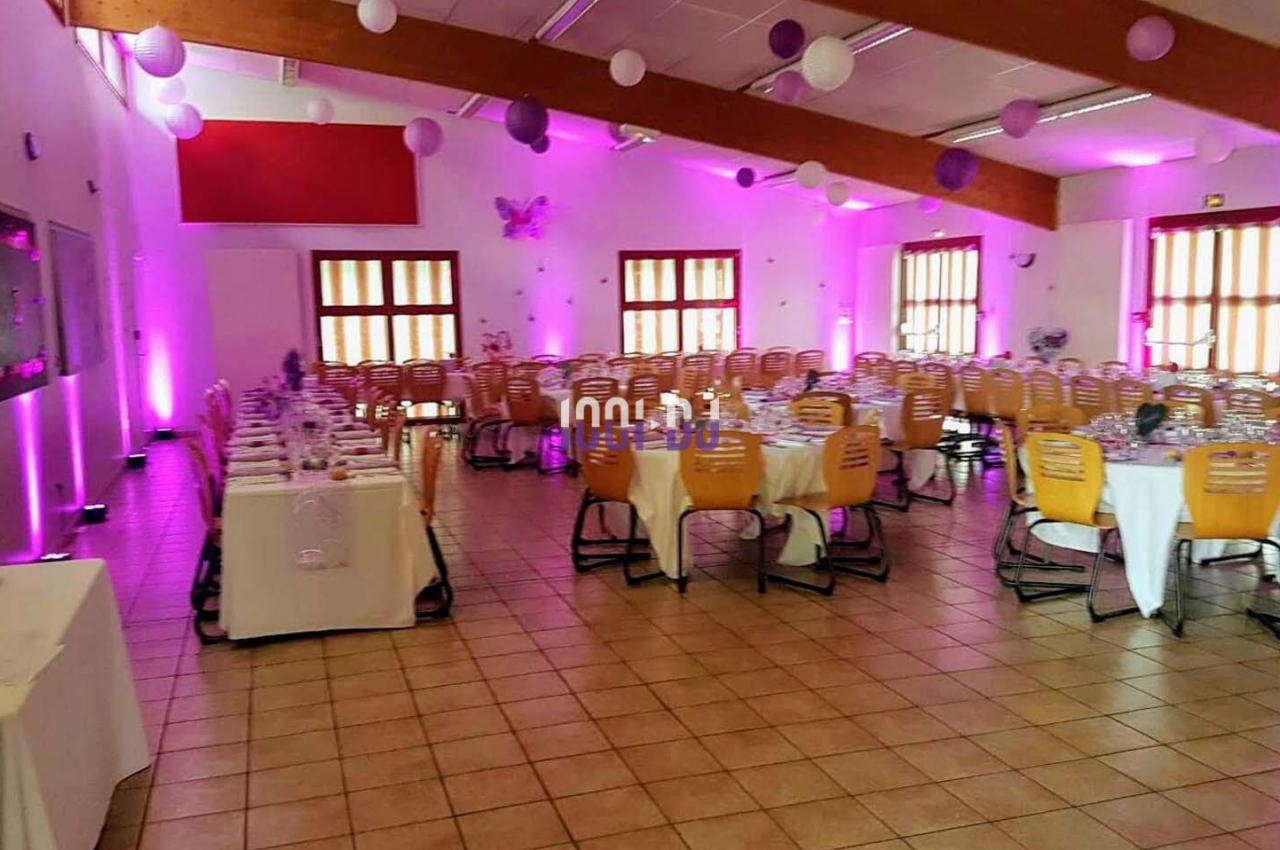 Salle de réception décorée avec des tables dressées, des chaises en bois et des guirlandes de ballons suspendues.
