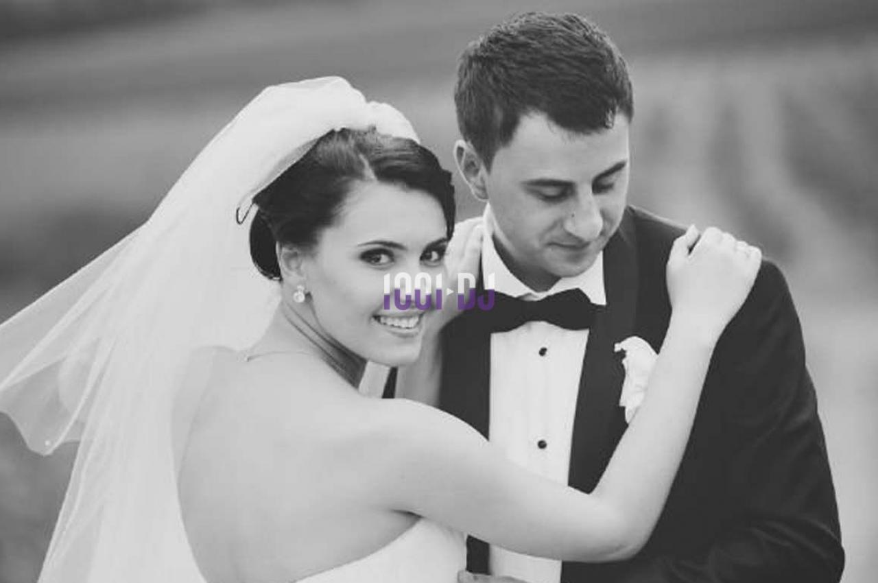Un couple en tenue de mariage pose en extérieur, la mariée souriante regarde la caméra.