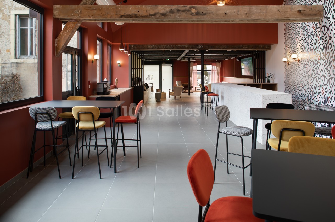 Salle lumineuse avec poutres apparentes, mobilier coloré et comptoir blanc, aménagée pour des espaces de travail ou détente.