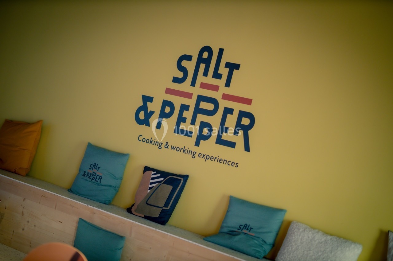 Mur jaune avec le logo ’Salt & Pepper’ et des coussins colorés disposés sur une banquette en bois.