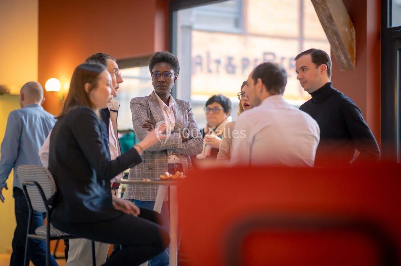 Un groupe de personnes discute debout autour d'une table haute dans un espace intérieur lumineux.