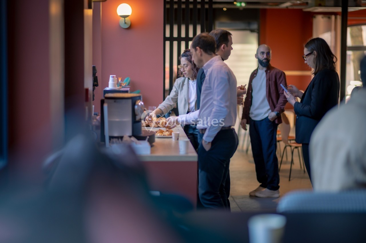 Des personnes discutent et se servent des viennoiseries près d'une machine à café dans un espace convivial.