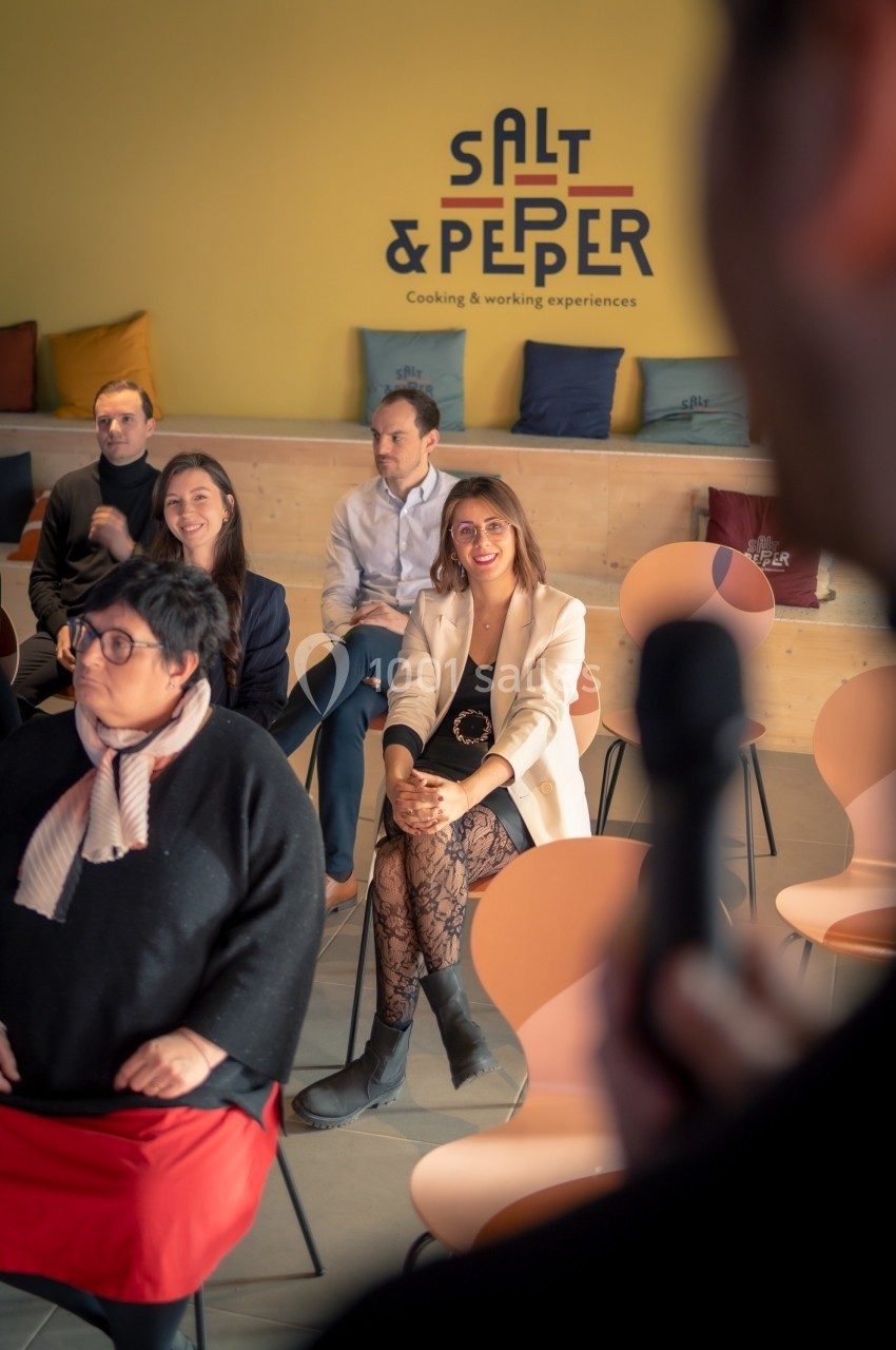 Personnes assises dans une salle lors d'une présentation, avec un intervenant tenant un micro au premier plan.