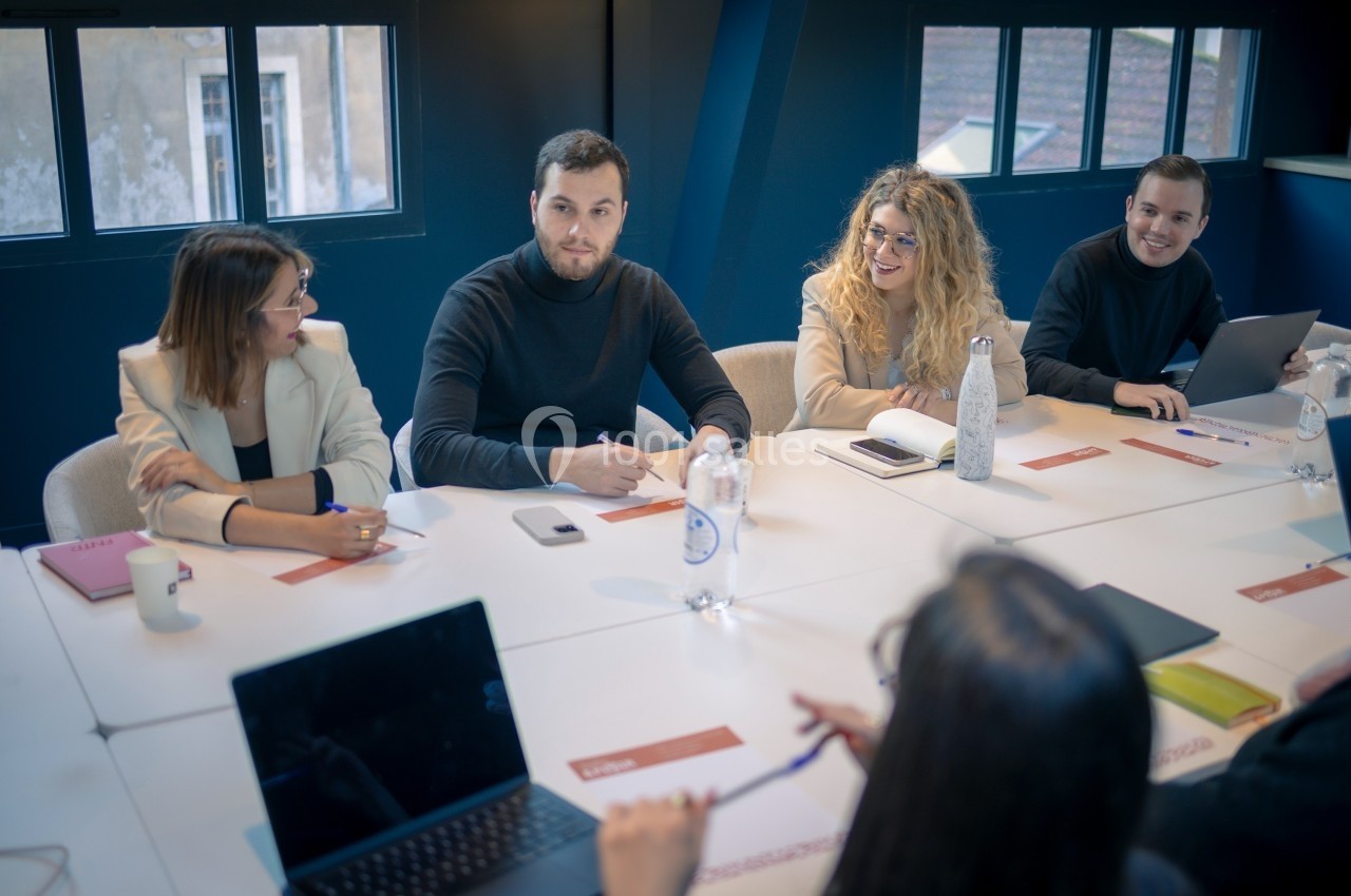 Un groupe de personnes discute autour d'une table de réunion, avec des documents et ordinateurs portables.