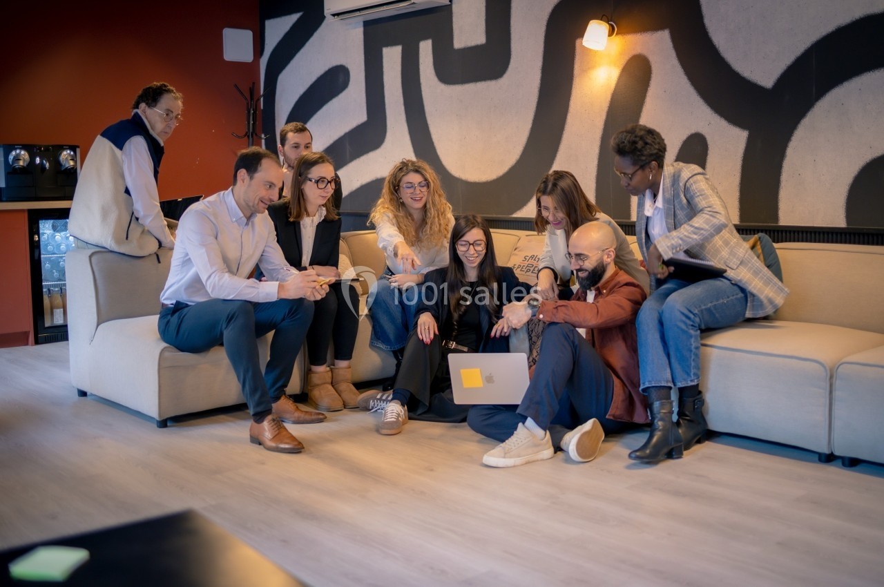 Un groupe de personnes assises sur un canapé et au sol, échangeant autour d'un ordinateur portable dans un espace moderne.