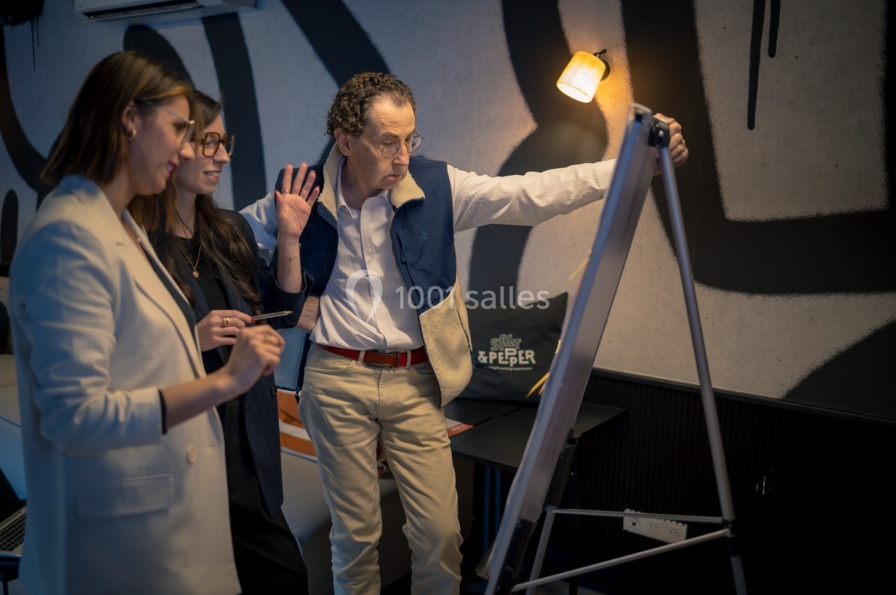 Trois personnes discutent devant un tableau blanc dans une salle avec un éclairage tamisé.