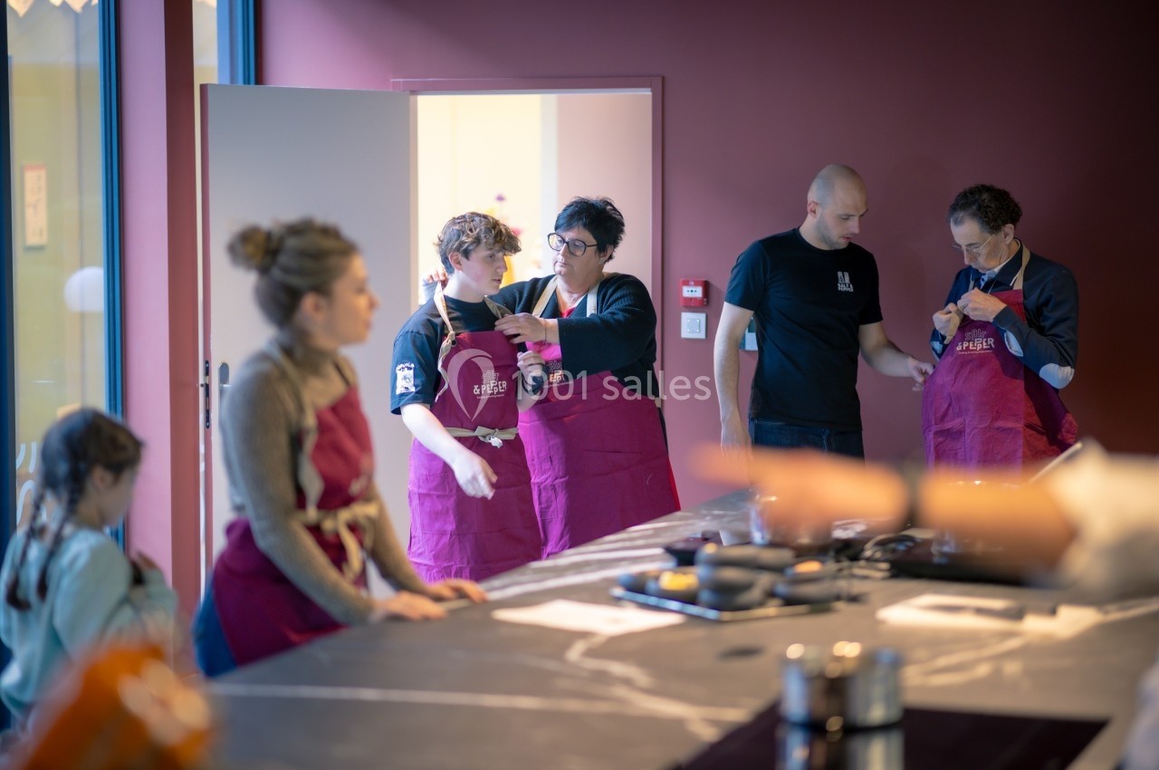 Des personnes en tabliers discutent et préparent une activité culinaire dans une cuisine moderne.