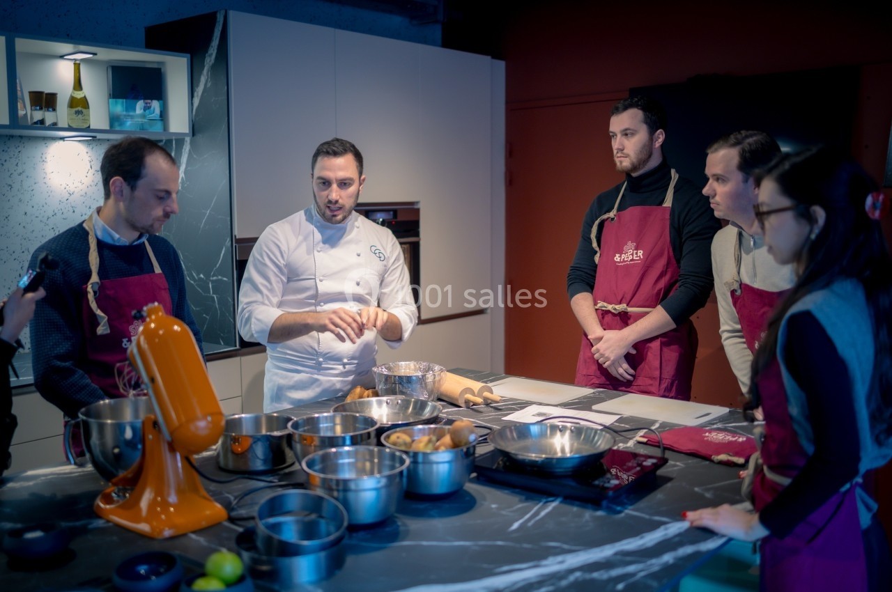Un chef pâtissier enseigne des techniques culinaires à un groupe de participants dans une cuisine moderne.
