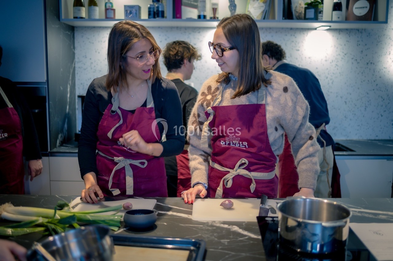 Deux femmes en tablier rouge discutent en préparant des ingrédients dans une cuisine moderne.