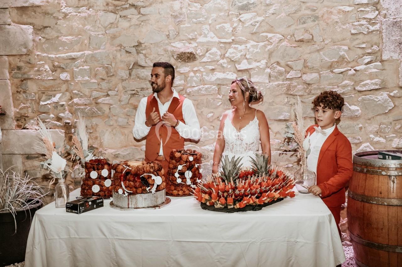 Un couple et un enfant devant une table décorée avec des desserts et des fruits, dans un cadre en pierre.