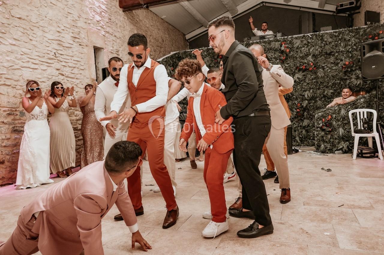 Des hommes et un enfant dansent ensemble sur une piste lors d'une fête, entourés de spectateurs applaudissant.