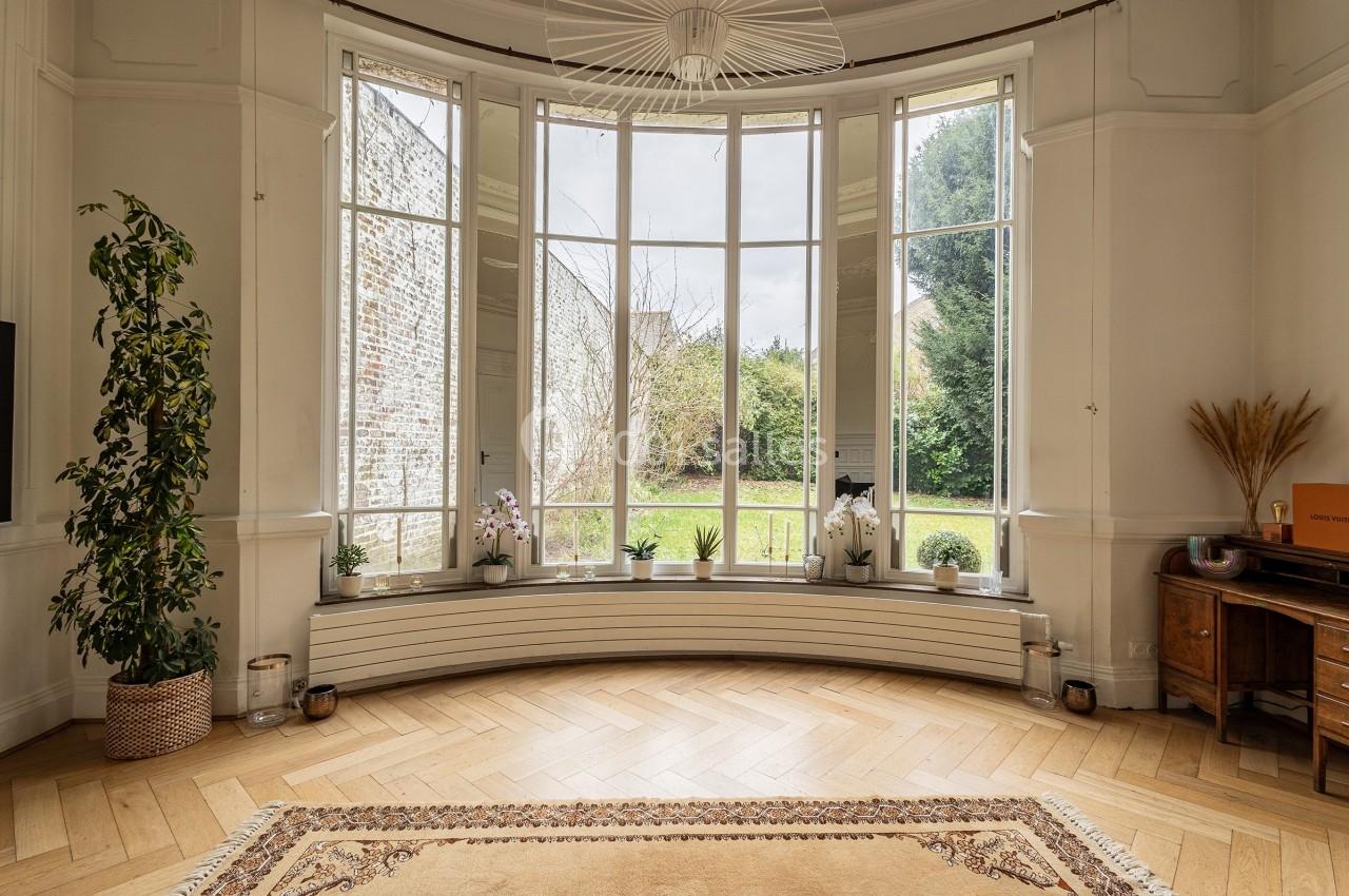 Grande baie vitrée arrondie donnant sur un jardin, entourée de plantes et d'un parquet en bois clair.