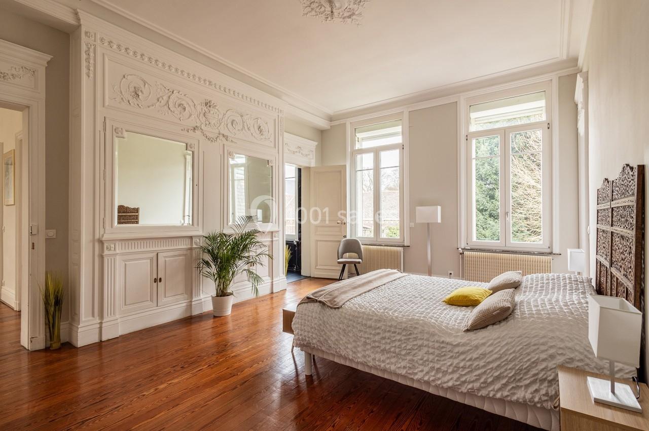 Chambre lumineuse avec parquet, lit double, moulures décoratives, miroirs et grandes fenêtres donnant sur un jardin.