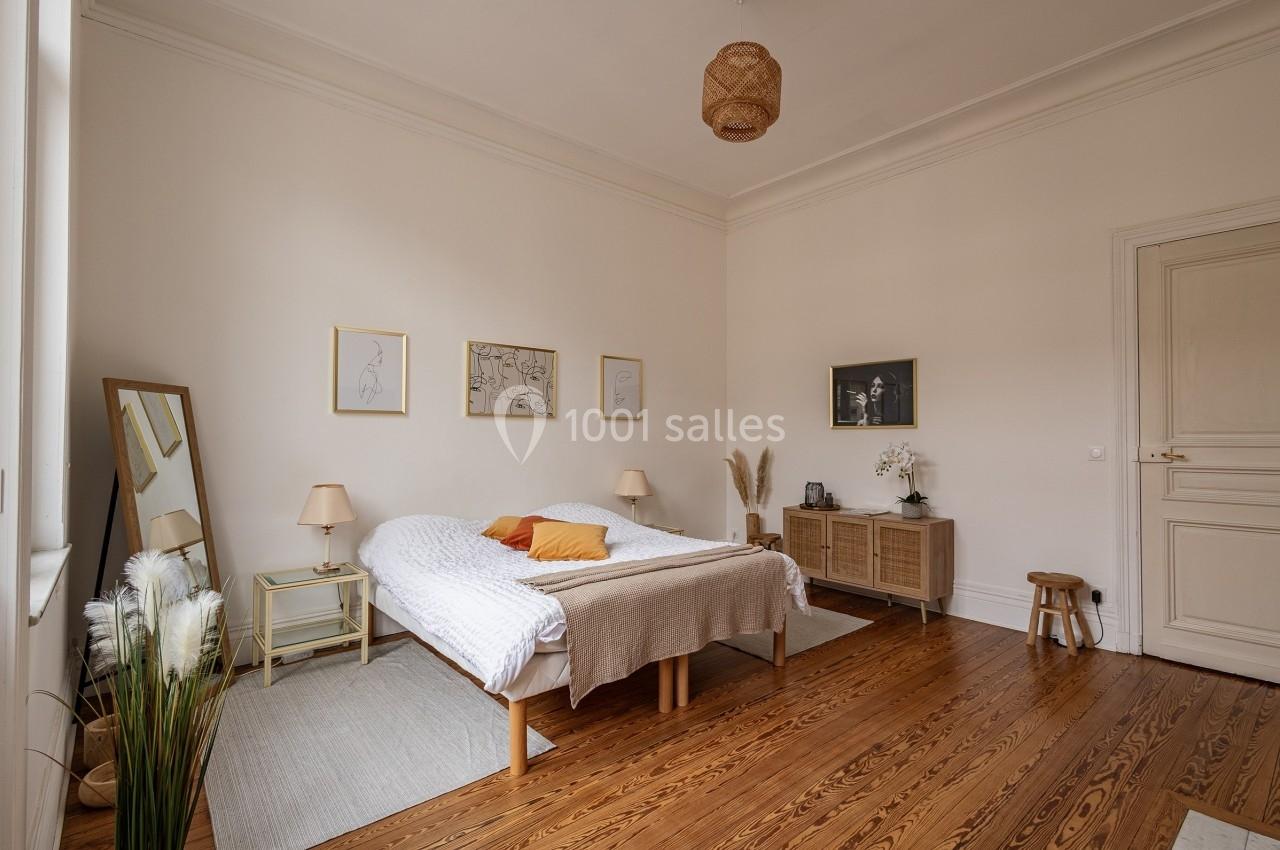 Chambre lumineuse avec lit double, parquet en bois, meubles en rotin, décor minimaliste et cadre épuré.