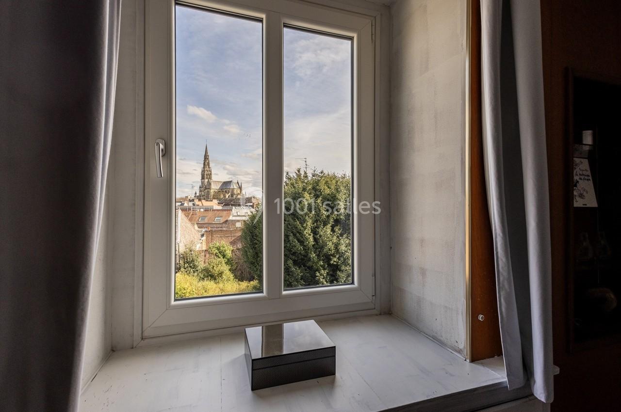 Vue depuis une fenêtre ouverte sur un paysage urbain avec une église en arrière-plan et des arbres au premier plan.