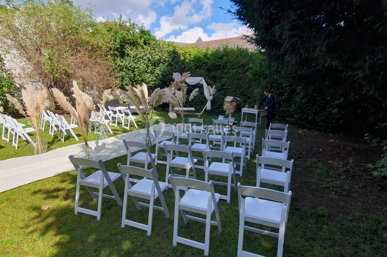 Chaises blanches disposées en rangées sur une pelouse, avec une allée centrale et une décoration florale en arrière-plan.