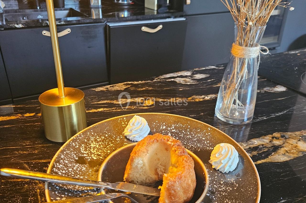 Dessert individuel avec crème chantilly sur une assiette, posé sur un plan de travail sombre avec une lampe et un vase.
