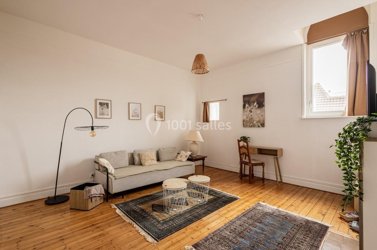 Salon lumineux avec parquet en bois, canapé gris, tapis, bureau en bois, et décoration murale minimaliste.