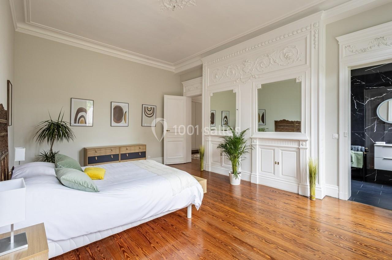 Chambre lumineuse avec parquet en bois, lit double, plantes décoratives et moulures blanches sur les murs.