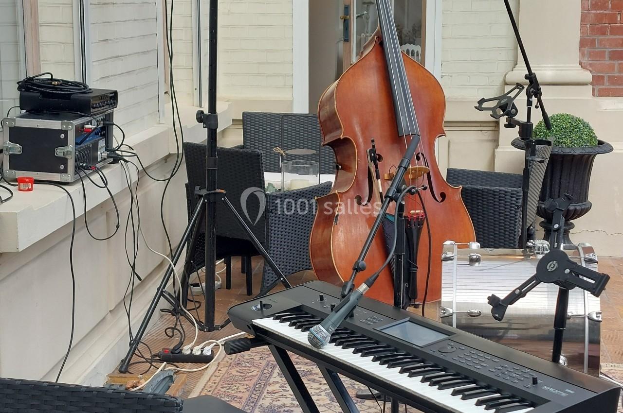 Clavier, contrebasse et matériel audio installés en extérieur sur une terrasse, prêts pour une performance musicale.