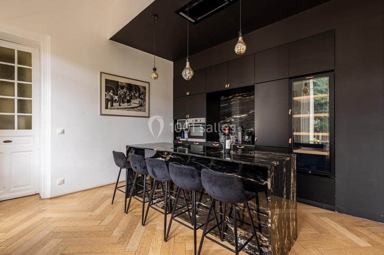 Cuisine moderne avec îlot central en marbre noir, tabourets, luminaires suspendus et appareils intégrés.