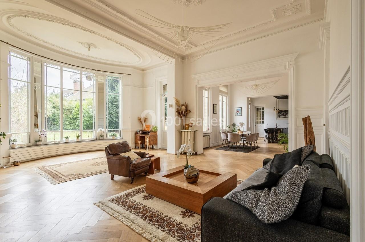 Salon lumineux avec parquet en bois, grandes fenêtres, mobilier élégant et vue sur un jardin verdoyant.