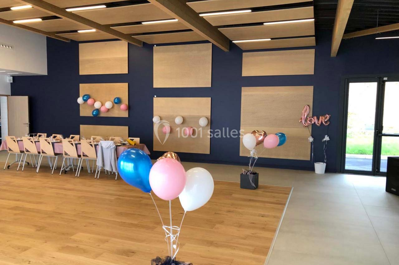 Salle décorée avec des ballons colorés et des guirlandes sur un mur bleu, prête pour un événement festif.