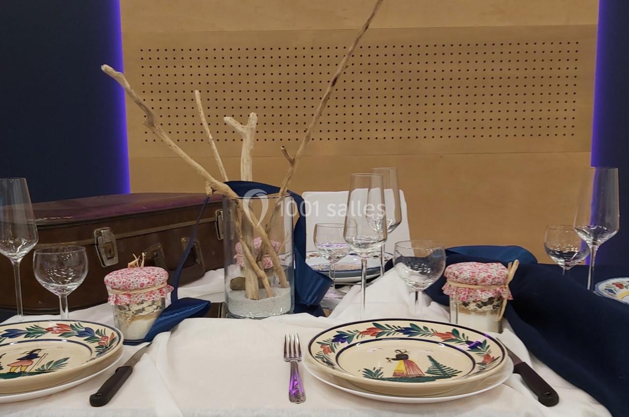 Table dressée avec vaisselle colorée, verres à pied, décorations en bois et pots ornés de tissu fleuri.