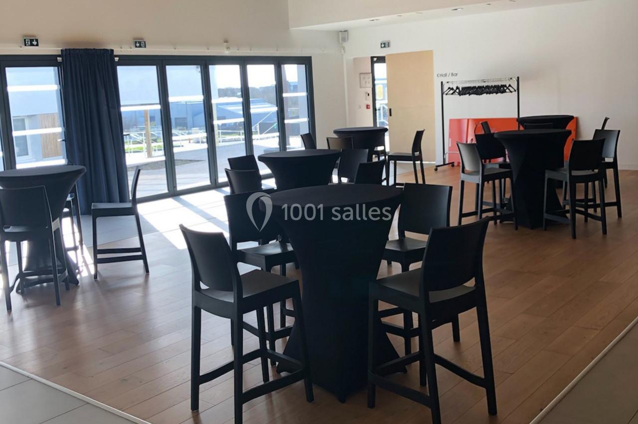 Salle lumineuse avec tables hautes noires, chaises assorties et grandes baies vitrées donnant sur une terrasse.