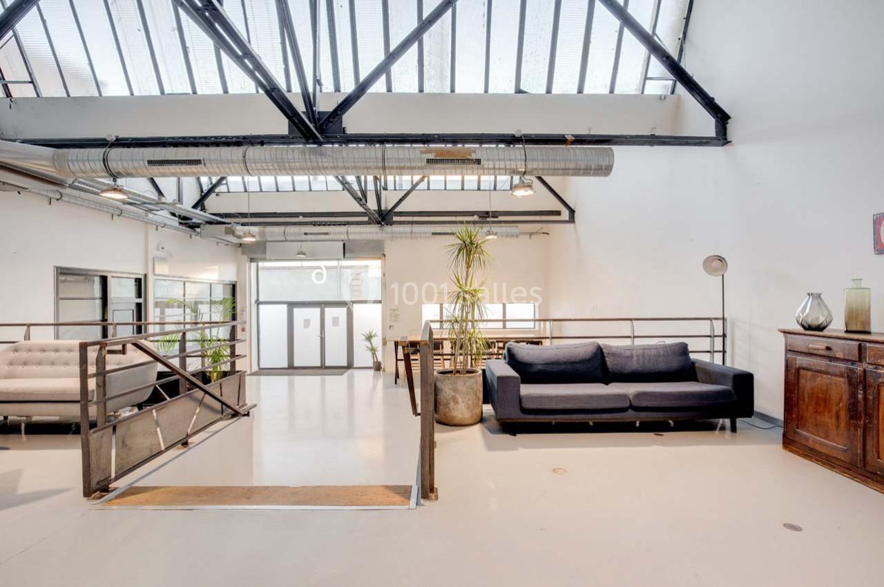 Espace lumineux avec verrière, canapé, plantes et mobilier en bois, dans un intérieur au style industriel.