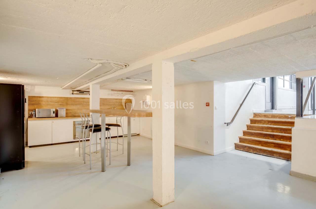 Cuisine ouverte avec comptoir en bois, tabourets hauts, électroménager moderne et escalier menant à une porte vitrée.