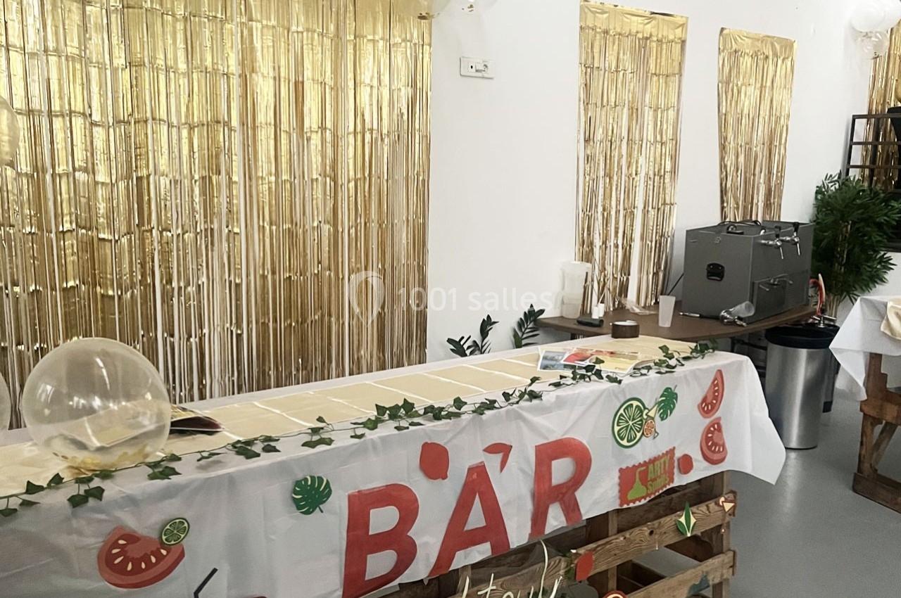 Table de bar décorée avec une nappe blanche, des motifs de fruits et des guirlandes, devant un fond doré scintillant.