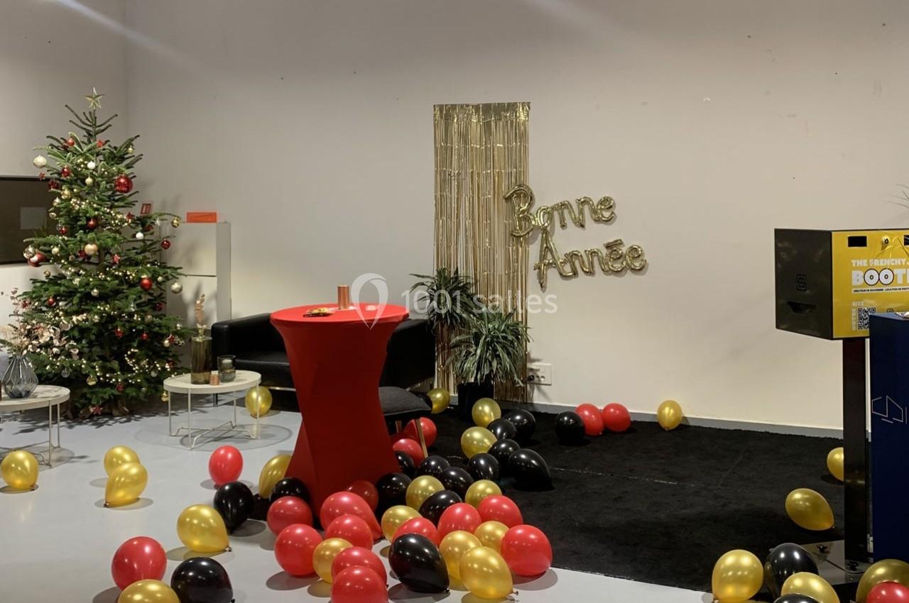 Salle décorée pour le Nouvel An avec un sapin, des ballons rouges, noirs et dorés, et une bannière ’Bonne Année’.