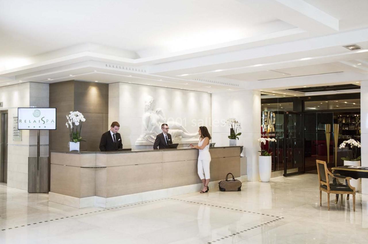 Réception d'un hôtel avec deux employés accueillant une cliente dans un hall lumineux et moderne.