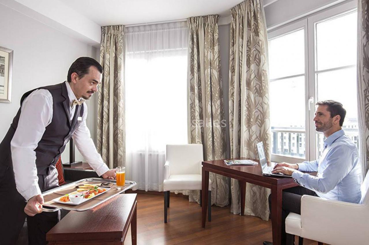 Un serveur apporte un plateau-repas à un homme travaillant sur un ordinateur dans une chambre lumineuse.