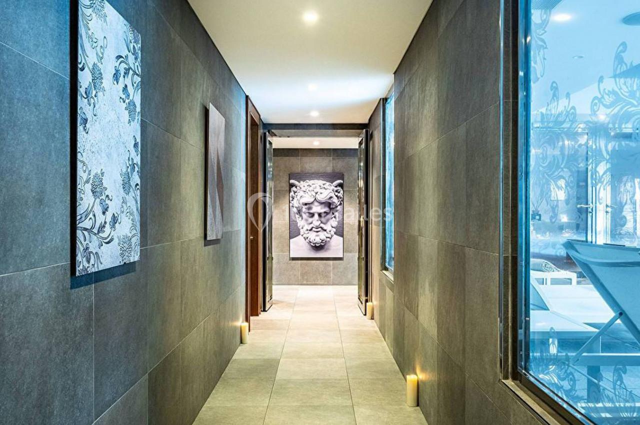 Couloir moderne avec murs en carrelage sombre, tableaux décoratifs et lumière douce, donnant sur une salle vitrée.