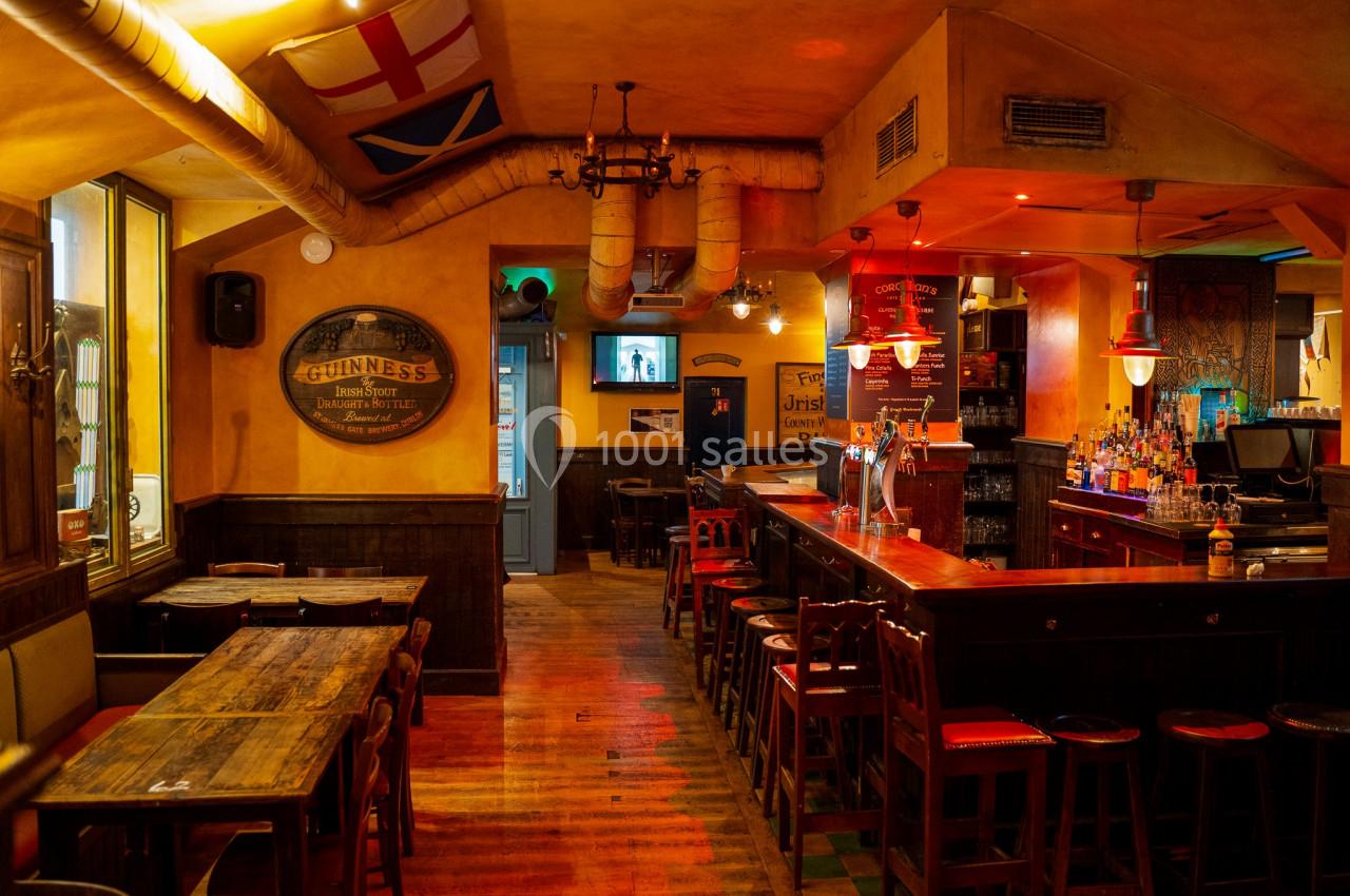 Location salle Paris 2 (Paris) - Corcoran's Grands Boulevards #3 Intérieur d'un pub chaleureux avec un bar en bois, des tables, des chaises et des drapeaux accrochés au plafond.