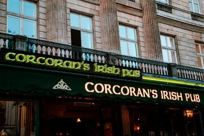 Miniature Location salle Paris 2 (Paris) - Corcoran's Grands Boulevards #12 Façade d'un pub irlandais avec enseignes lumineuses vertes et jaunes, devant un bâtiment en pierre.