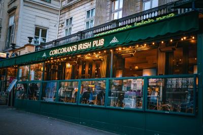 Miniature Location salle Paris 2 (Paris) - Corcoran's Grands Boulevards #10 Façade d'un pub irlandais avec enseignes lumineuses vertes et jaunes, devant un bâtiment en pierre.