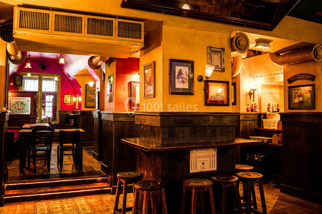 Intérieur d'un bar chaleureux avec des tables en bois, des tabourets et une lumière tamisée.