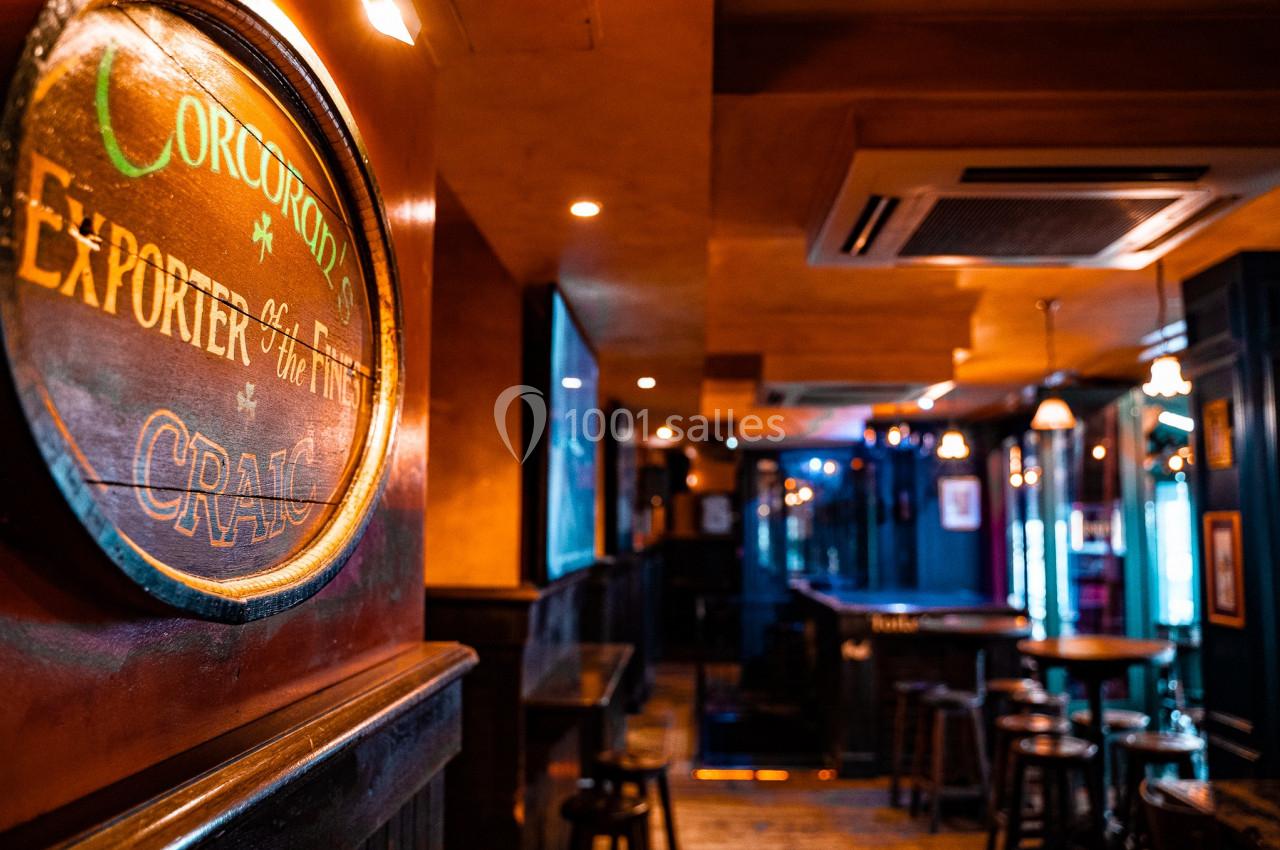 Intérieur d'un pub chaleureux avec éclairage tamisé, tables hautes et enseigne murale en bois.