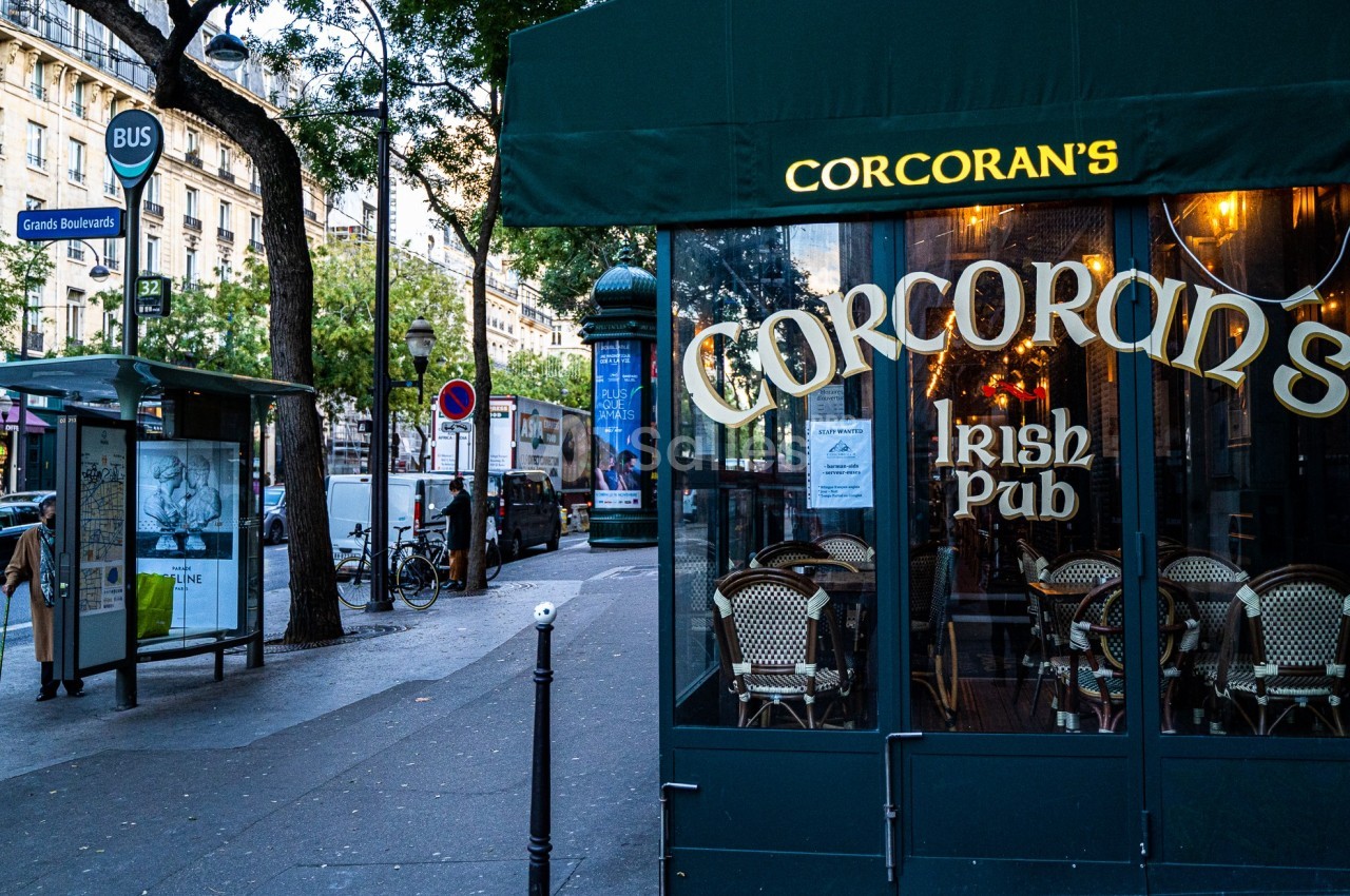 Façade d'un pub irlandais avec terrasse, situé près d'un arrêt de bus dans une rue animée.
