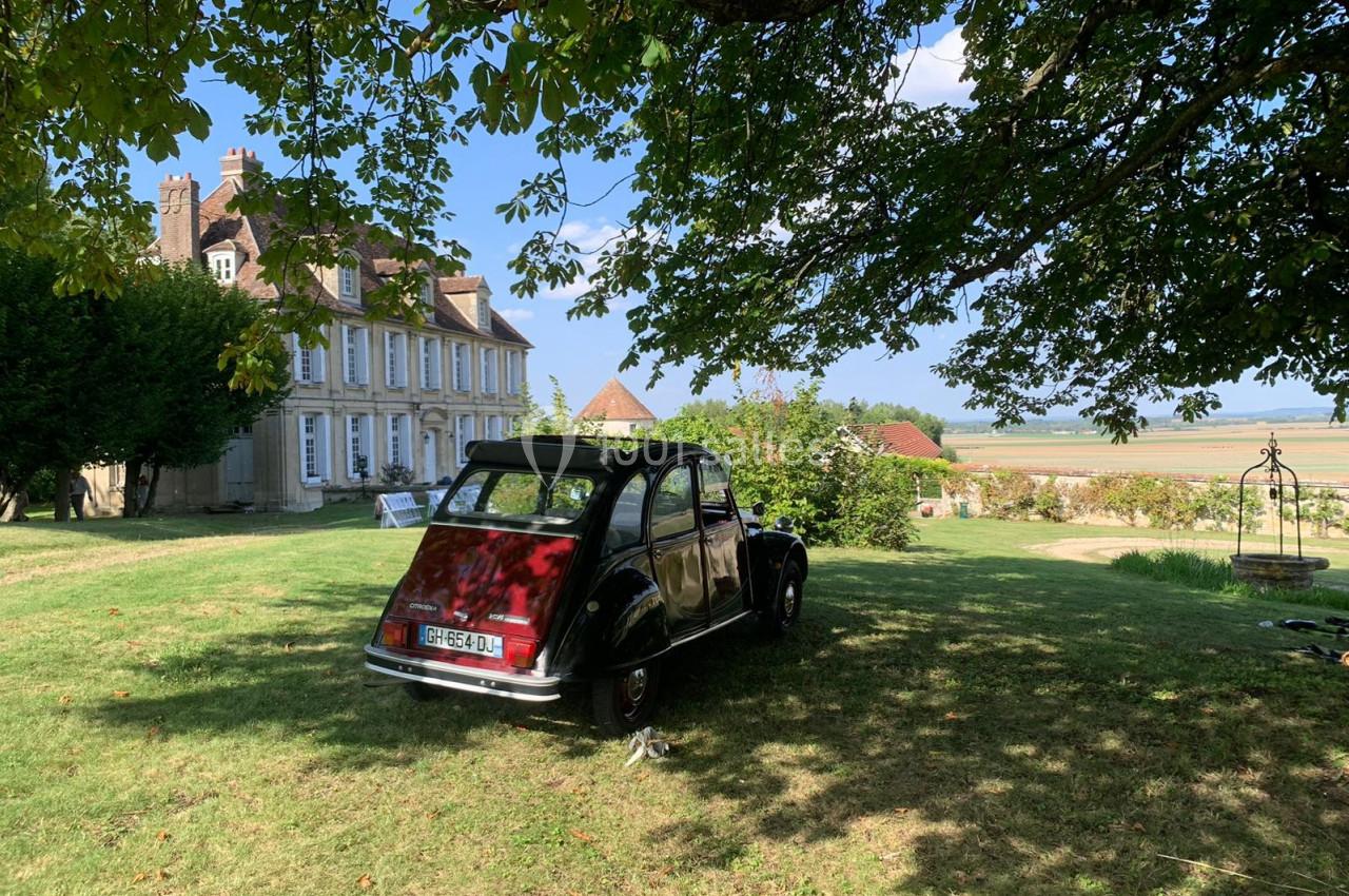 Location salle Wy-dit-Joli-Village (Val-d'Oise) - Château d'Hazeville #20 Une voiture ancienne garée sur une pelouse ombragée devant une maison de campagne avec vue sur un paysage rural.