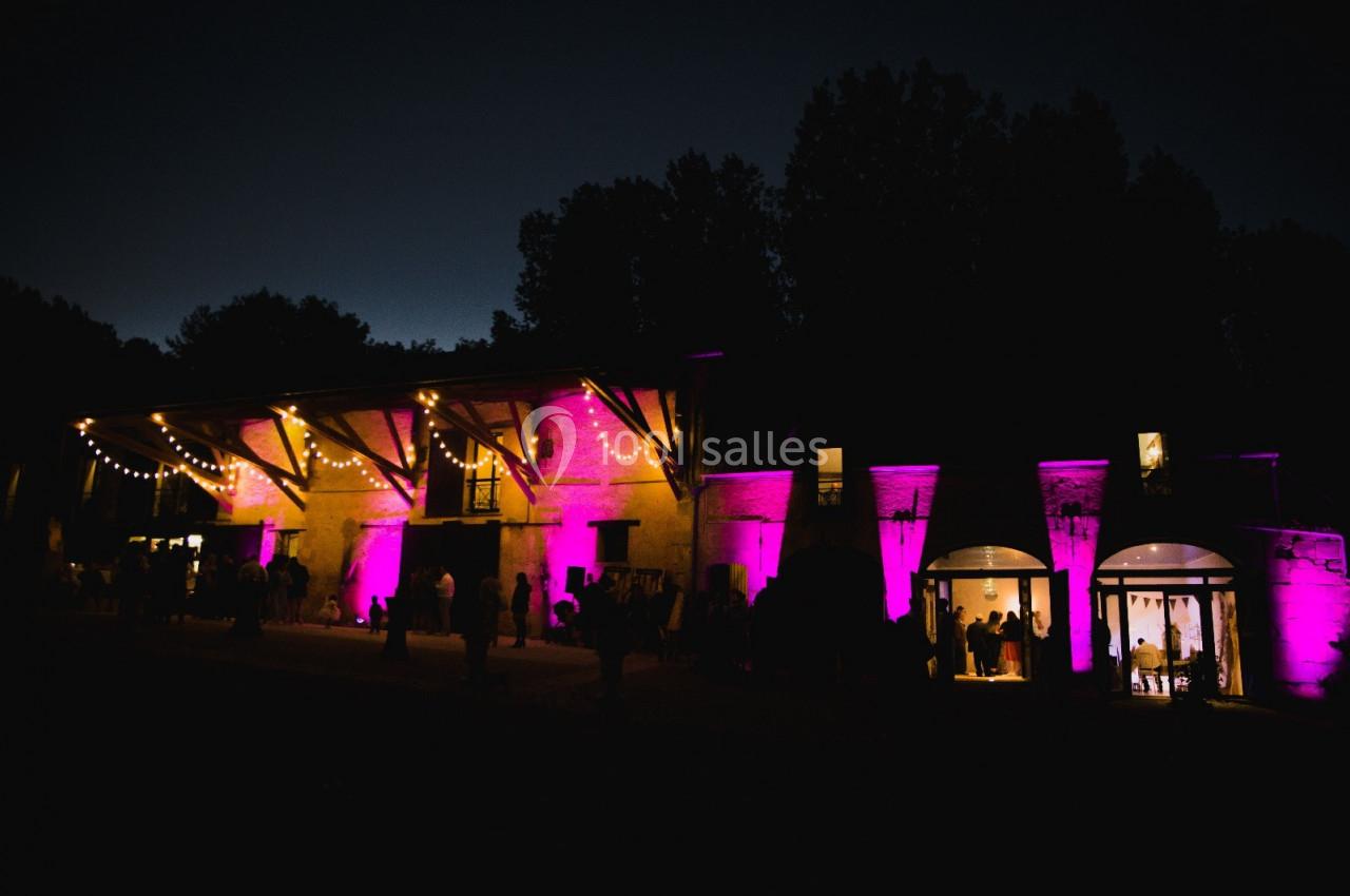 Location salle Wy-dit-Joli-Village (Val-d'Oise) - Château d'Hazeville #7 Bâtiment éclairé par des lumières violettes et guirlandes lumineuses, avec des silhouettes de personnes à l'extérieur, de…