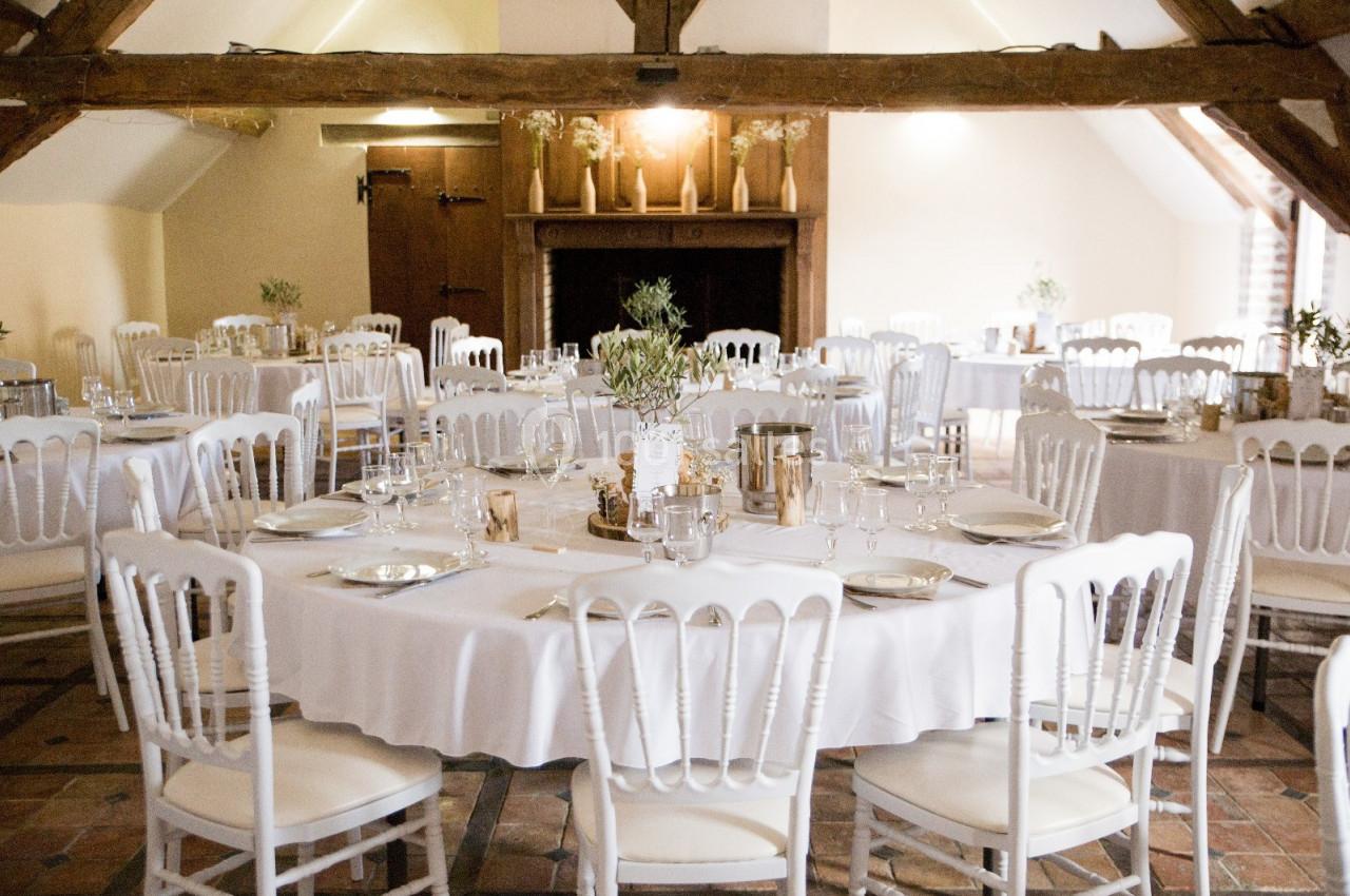 Location salle Wy-dit-Joli-Village (Val-d'Oise) - Château d'Hazeville #13 Salle de réception lumineuse avec tables rondes dressées, nappes blanches et chaises assorties sous une charpente en bois.